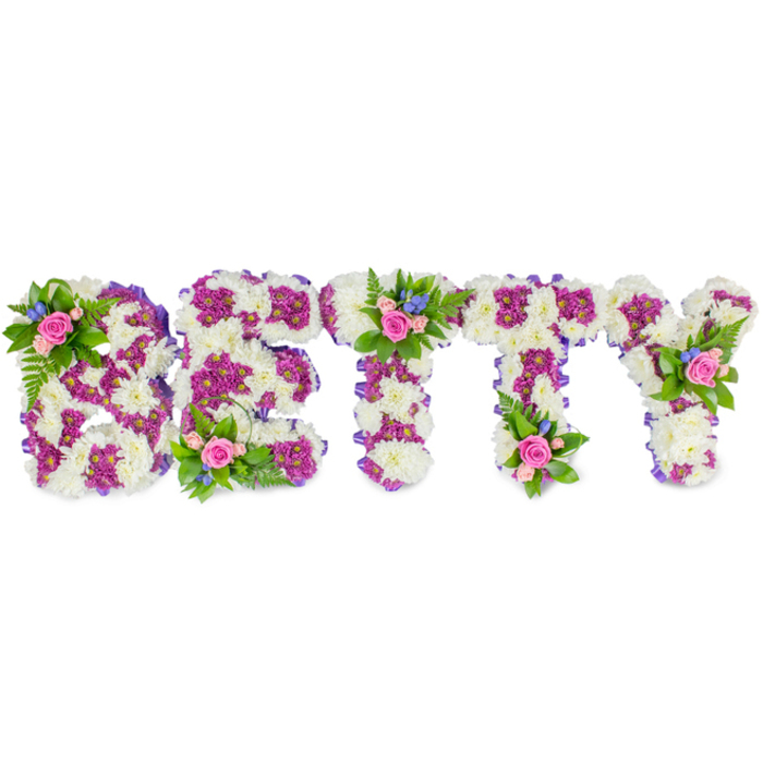 This personalised floral tribute spells the name BETTY in bold uppercase letters, each letter sculpted from a dense layer of soft white chrysanthemums that create a pillowy, tactile surface reminiscent of freshly fallen snow. Set against a stark white background, the design relies on colour contrast to read clearly: clusters of vivid magenta or deep purple chrysanthemums form defining patterns inside and around each letter, accentuating the loops of the B, the bars of the E, and the cross-piece of each T with a refined, almost calligraphic clarity. Along the perimeters, a narrow purple ribbon subtly frames every character, giving the whole piece a neat, finished look. On the B's upper curve, at the centre of the first T and on the Y's upper arm, small decorative bouquets are artfully placed-each containing soft pink roses from bud to bloom, tiny bright blue filler flowers (likely delphinium or cornflower), and sprigs of fresh green fern-like foliage. These mini-bouquets introduce a tender human touch, their rose scent rounding the crisper chrysanthemum notes and the greenery adding an earthy, garden-fresh undertone. Meant to rest on a service table or be positioned at the front of a chapel, the arrangement conveys reverence and warmth; its colours-white, purple, pink and blue-speak of remembrance, dignity and gentle celebration. Local families in Grove Park and surrounding streets often choose this style when they want a clearly personalised, handcrafted tribute that honours a life with both simplicity and artisan skill.