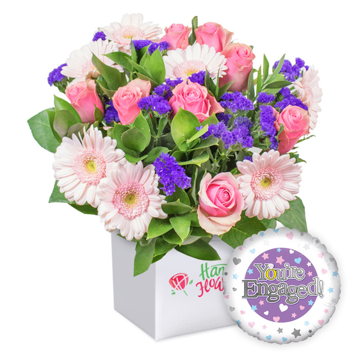 Near the quiet lanes of Grove Park, this elegantly jaunty bouquet speaks of celebration and bright futures. The arrangement sits in a pristine white square box, its lines clean enough to suit a modern living room, yet warm enough to feel welcoming at a doorstep. Soft pink roses take the lead, their petals opening to reveal delicate spirals of blush against the stems, a timeless symbol of affection. They mingle with pastel pink gerbera daisies, their round blossoms edged in white and pale yellow centers giving the bouquet a soft, sunlit glow. A generous scattering of purple filler blooms threads through the display, adding depth and a hint of mystery to the palette. The greenery-broad, satin, and feathery leaves-creates a lush, organic frame that makes the entire arrangement feel garden-fresh. The presentation box is complemented by a small, refined red rose motif, hinting at quality and care without distracting from the florals. To the lower right, a round foil balloon completes the gift set, its surface a gentle lavender tone with a central purple circle containing the silver lettering 'You're Engaged!', the O cleverly shaped as a golden engagement ring. A ring of tiny pastel hearts and silver stars around the circumference adds charm and whimsy. This bouquet, ideal for a newly engaged couple, feels like a bright beginning-perfect for delivery to Grove Park homes, offices, or celebrations, and it pairs beautifully with a toast and a card of warm wishes.