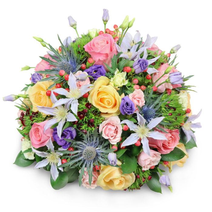 This lavish, dome-shaped bouquet is photographed against a spotless white background, its form casting a very soft shadow that emphasises its fullness while keeping every detail crisp and visible. The arrangement itself is densely composed, evoking the feeling of a garden gathered at its peak, as if carefully selected from the flourishing greenery around Grove Park. Dominating the bouquet are plush garden roses in a palette of blush pink, sunny yellow, and creamy peach, their petals layered in generous spirals. Some roses are wide open and frilled, revealing their centres, while others remain more tightly closed, giving a sense of gentle movement and life. Interspersed among them are ethereal clematis blooms, their star-shaped petals in shades of white and pale lavender stretching outward from contrasting yellow or white centres that add small bursts of brightness. To offset this softness, distinctive blue Eryngium, or sea holly, rises with metallic blue-grey, spiky heads, lending a slightly wild, contemporary edge that brings to mind the textured plantings seen in local riverside gardens. Deep purple lisianthus blooms weave throughout the design, from closed, ruffled buds to half-opened flowers, providing velvety shadows and richer tones within the pastel mix. Clusters of bright red Hypericum berries punctuate the bouquet, their tiny, rounded, and glossy forms adding cheerful specks of colour and a pleasing variation in texture. A bed of varied green foliage supports and frames the flowers: broad, polished leaves create structure, while lighter, feathery greens and hints of dark burgundy foliage weave in and out, creating depth, shadow, and a slightly woodland feel. The soft, even lighting highlights the careful craftsmanship of the arrangement, which would be equally at home as a centrepiece for an intimate dinner in Grove Park or delivered as an elegant gesture of sympathy or congratulations.