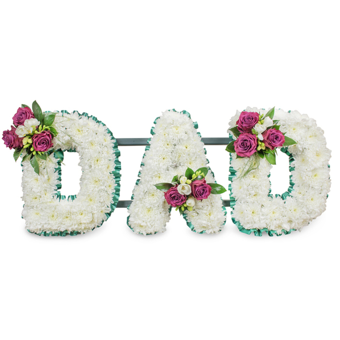 A deeply considered sympathy tribute spells DAD in bold, capital letters, each letter built from a luxurious mass of small white chrysanthemums that together form a continuous, cloud-like surface. The letters are sharply defined with an emerald green, pleated ribbon that traces both outer and inner edges, the crisp ruffling offering a composed contrast to the soft white blooms. Three accent clusters of saturated magenta roses break the white canvas: velvety rosebuds and half-open blooms sit beside tiny white freesia or delicate spray flowers and glossy dark-green foliage, lending textural variety and a quiet lift of colour. The decorative clusters are sited with careful balance - upper left of the first D, cradled in the lower V of the A, and upper right of the final D - creating a visual rhythm that reads clearly from the front pew. A subtle dark-green or grey support bar runs horizontally behind the letters, suggesting a stable, self-supporting display appropriate for a chapel, funeral cortege or graveside at times of remembrance. In clean lighting the chrysanthemums' soft surfaces catch gentle shadows while the roses offer faint, familiar perfume; the green ribbon gleams with a composed sheen. As an experienced florist serving Grove Park, Lewisham and the surrounding neighbourhoods, I see this piece as a classic, personalised expression of love and respect - quiet, tactile and thoughtfully constructed to honour a father figure during a tender farewell.