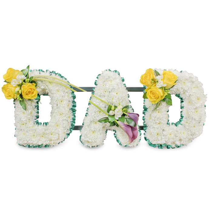 A striking, bespoke funeral tribute spelling out DAD in three-dimensional letters, each letter composed of a compact mass of pristine white spray chrysanthemums that read as a soft, even surface from a few paces and reveal layered texture close up. The contours of every letter are neatly finished with a ruffled, deep green satin ribbon or foliage trim that gives the shapes a crisp edge and a refined contrast to the white blooms. Behind the letters, discreet dark green metal support bars are visible, joining the three pieces into a unified memorial display and giving the arrangement the stability required for public viewing in a chapel or crematorium. On the upper curve of each D sits a joyful cluster of bright yellow roses-typically three to four blooms-complemented by tiny white freesias and lush green leaves, a pairing that creates a warm, hopeful accent against the sober white. The central A is accentuated lower on its diagonal by two dramatic calla lilies in a deep purple to burgundy, their trumpet forms adding an elegant, almost architectural counterpoint to the rounded letters. Long, bare green stems arch between clusters, creating an intentional line that guides the eye across the tribute. The overall mood is respectful and composed, combining purity, affection and reverence; crafted with local knowledge for families in Grove Park, Lewisham and surrounding Hither Green and Lee, this arrangement communicates a quiet, personal farewell through careful floristry.