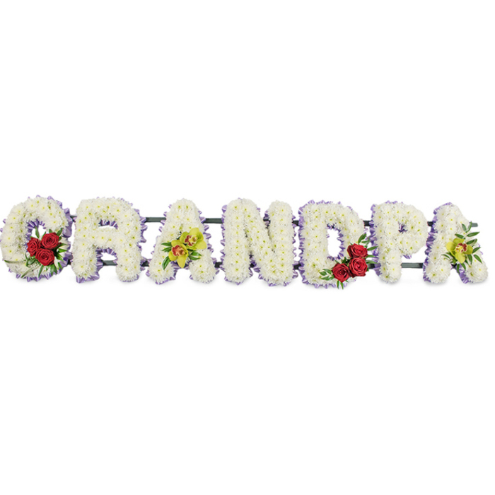 In this image, the word GRANDPA is rendered as a long, horizontal floral tribute, designed to sit proudly beside a coffin or at the front of a chapel in Grove Park. Each letter is built up in a solid block style and then completely covered with pristine white chrysanthemums, leaving no bare spaces. The flowers are compact and plentiful, their many small petals giving the surface a soft, quilted appearance. The clean white of the blooms is set off by a slim, continuous edging of pale lavender ribbon that runs along the perimeter of each capital, lending a gentle, pastel frame which helps the letters stand out distinctly from the white background. At the start of the word, inside the curve of the G, there is an accent of deep red roses, three or four blooms gathered with dark green foliage. The roses' rich, velvety petals provide a striking contrast to the cool white chrysanthemums, evoking sentiments of love, gratitude, and the warmth of family gatherings. The first A is decorated with a cluster of yellow-green orchids, their unusual colour and elegant shape giving the tribute a modern, refined note. A little further along, in the D, another group of red roses echoes the arrangement in the G, creating visual balance and a sense of continuity. The final A mirrors the earlier orchid accent, displaying a small spray of those same yellow-green blooms, some with soft reddish details in the throat. Discreet metal bars join the letters from behind, ensuring that the word reads clearly as one complete tribute. The lighting is even and gentle, with minimal shadows, enhancing the calm, respectful atmosphere. As might be created by Grove Park Florist for services in local churches or at nearby crematoria, this arrangement conveys a heartfelt farewell and lasting remembrance for a beloved grandfather.