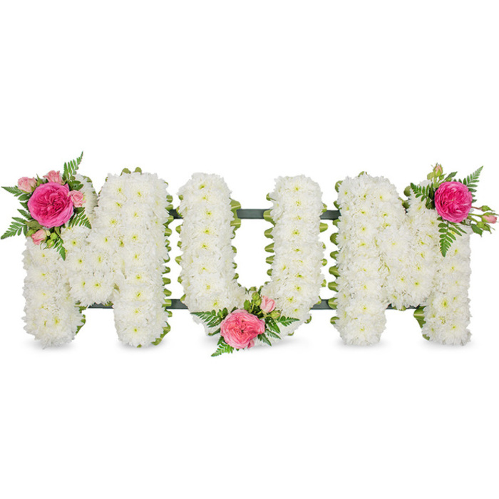 A touching floral tribute in the photograph spells out the word MOM in firm, capital letters, elegantly displayed against a plain white background that emphasises its form and colour. Each of the three letters is completely enveloped in tight clusters of small white flowers, likely chrysanthemums, whose rounded, petal-filled heads press together to form a uniform, cushion-like texture. This unbroken expanse of white suggests serenity and reverence, a quiet visual echo of the calm atmosphere found in Grove Park's residential streets and riverside walks. At the base of the letters, a dark green metal or plastic bar and framework can be glimpsed, giving structural integrity and a hint of contrast, like a subtle underline that supports the sentiment expressed by the word. To avoid starkness and to personalise the tribute, the florist has added three carefully placed clusters of coloured blooms. On the top left of the first M, a vivid fuchsia rose unfolds among paler pink roses and delicate fern fronds, the greenery extending in fine, lace-like patterns that soften the rigid line of the letters. A second accent rests in the lower space between the O and the second M, combining the same pink roses and fresh foliage to create a focal point near the centre of the piece. The third cluster is positioned at the upper right of the final M, mirroring the first and completing a gentle diagonal line of colour across the arrangement. The tribute feels refined, traditional, and full of feeling, suitable for display during a funeral service in Grove Park or at a nearby crematorium, where its quiet beauty and carefully chosen flowers honour the memory of a devoted mother.