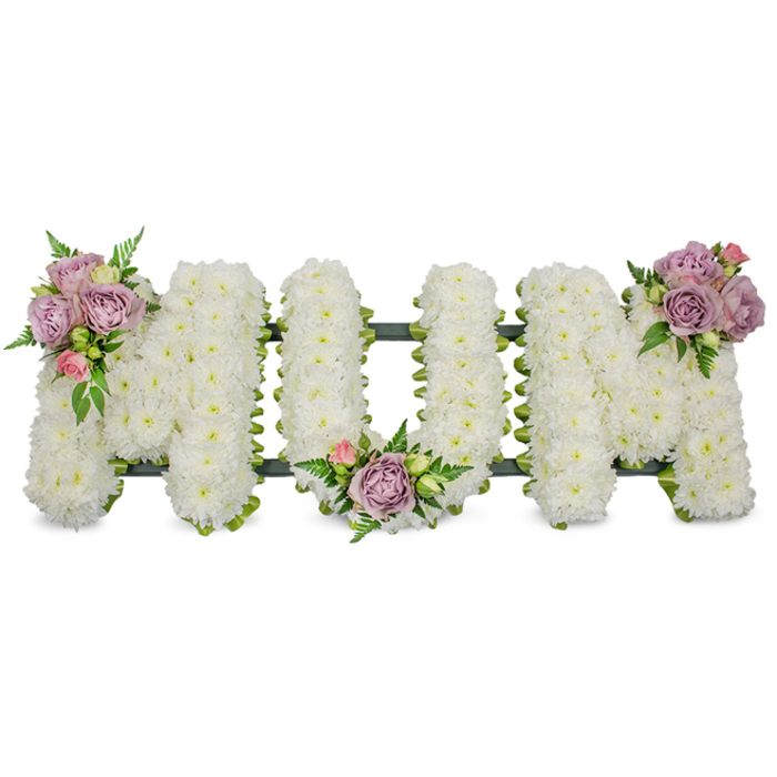 A carefully crafted, large-scale funeral tribute spells MUM in bold capitals, each letter densely covered with hundreds of fresh white spray chrysanthemums to produce a soft, cloud-like texture that reads as pure and serene against a brilliant white backdrop. Close inspection reveals three artful accent groupings of soft lavender and pale pink roses: one perched on the upper left arm of the first 'M', another tenderly placed in the curved base of the 'U', and a third embellishing the upper right of the final 'M'. The contrast between the crisp, snow-white chrysanthemums and the velvety pastel roses creates a gentle visual cadence; the roses' fragrance and the green foliage's earthy scent add a quiet sensory warmth. Interspersed fern fronds and small bright green leaves give depth and movement, subtly breaking the white field and framing each letter with living texture.A dark green structural band - whether ribbon-wrapped foam or mossed timber - is visible along the lower outline, a discreet, stabilising element that keeps the letters upright and unified. This composition is intended as a dignified personal tribute for a mother, balancing traditional formality with tender detailing. As a local arrangement offered near Grove Park - often delivered to services around Grove Park Station, Baring Road or to ceremonies by Chinbrook Meadows - this design reflects the careful workmanship Grove Park Florist brings to sympathy work: respectful, composed, and mindful of how floral memory sits within a community's quiet places.