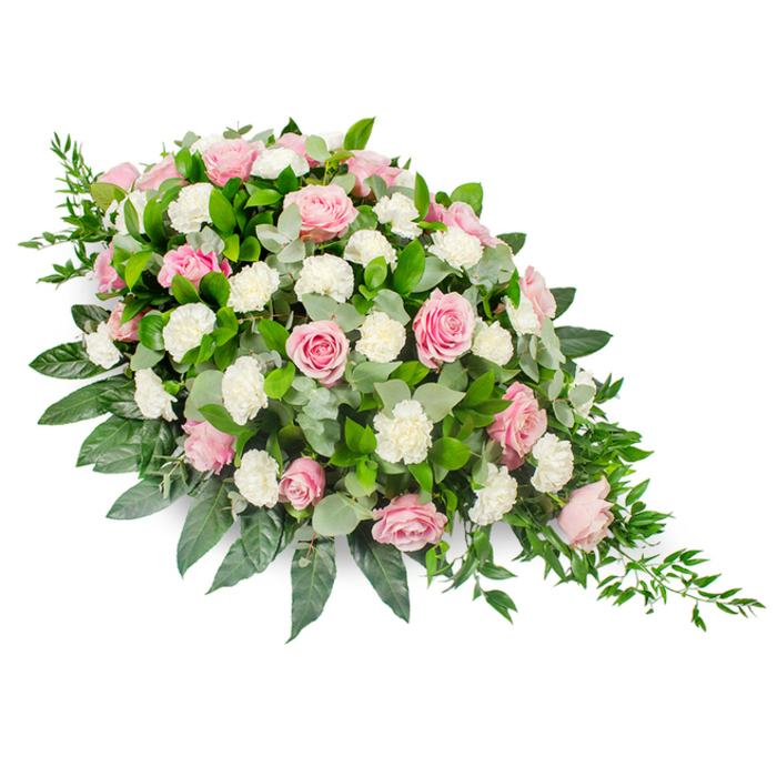 Photographed in clear, even light against a simple white background, this large sympathy spray reveals a carefully structured teardrop or casket-spray shape. The top section, broad and full, is richly adorned with soft pink roses that gradually lead the eye down the length of the design. Each rose is distinct: some stand tall and almost bud-like, while others open into wide, layered blooms that show off their velvety, overlapping petals. Threaded throughout are white carnations, their finely fringed petals forming rounded, cushiony blooms that add a gentle contrast in both texture and tone. Beneath and around the flowers, a substantial layer of dark green foliage spreads outward, its glossy surfaces catching the light and giving the spray a polished, finished look. Nestled among the darker leaves are smaller, rounded eucalyptus leaves in silvery-green, creating subtle pockets of cool colour and visual breathing space. From the tapered, narrow end of the arrangement, slender strands of trailing greenery extend and spill slightly outward, enhancing the sense of movement and drawing the teardrop outline to a delicate point. The effect is peaceful and composed, with soft pinks and whites evoking tenderness and remembrance, while the lush greens ground the design in nature. It is a tribute that feels at home in the quiet streets and leafy corners of Grove Park, suitable for placing on a coffin, at the front of a chapel, or near a memorial table during a service. The overall impression is one of dignity and gentle comfort, as if the flowers themselves are offering a final, heartfelt embrace.