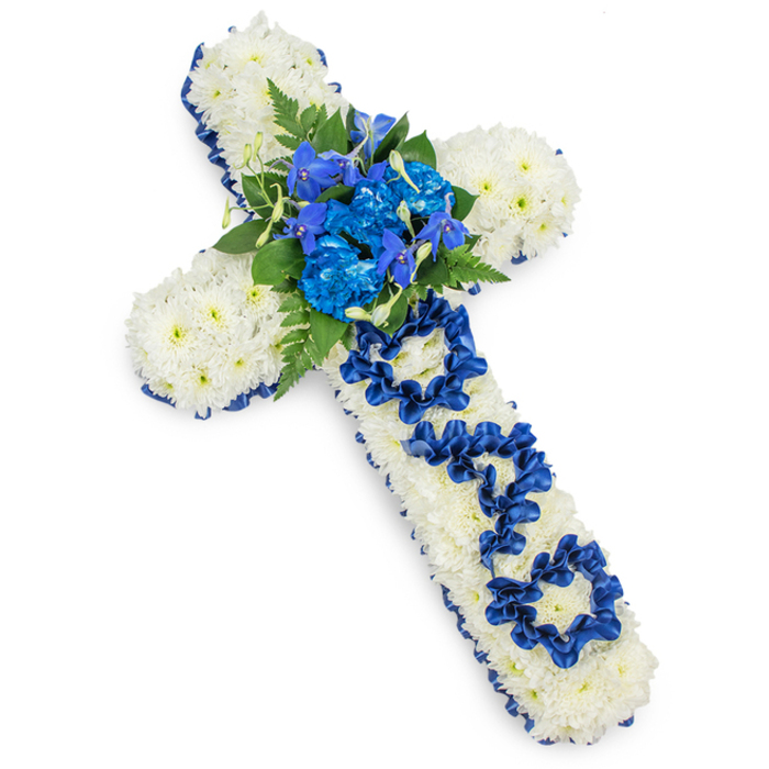 This image features a carefully crafted funeral cross laid on a seamless white background, allowing every element of the design to be clearly appreciated. The base of the cross is entirely made up of small white spray chrysanthemums, their rounded heads nestled tightly together so the surface appears soft, full, and completely carpeted. The pure white blooms provide a serene, almost luminous foundation. Framing this is a continuous border of royal blue satin ribbon, its clean folds hugging the contours of the cross and catching gentle highlights that bring a subtle sense of movement. At the crossing point of the arms, a central cluster of royal blue flowers draws the eye: full, frilled carnations and more delicate, upright blue florets, reminiscent of delphinium, are arranged together in a rich blend of textures. Dark green fern fronds and smooth leaves radiate around this focal area, providing contrast and giving the arrangement a natural, organic feel amid its structured form. Along the vertical arm, the word DAD has been lovingly shaped from the same dark blue ribbon, the letters sculpted and anchored into the white chrysanthemum cushion so that they are legible yet gentle in appearance. Soft, even light ensures that the interplay between satin ribbon, velvety petals, and glossy foliage is clearly visible, with a faint shadow beneath the cross hinting at its substantial construction. The overall impression is of a respectful, deeply personal tribute, the kind of floral cross a family in Grove Park might place in a chapel, at a crematorium, or beside a grave. Its cool blue and white palette suggests peace and remembrance, echoing the quiet, reflective character of the area's tree-lined avenues and riverside walks.