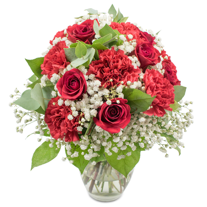 A richly detailed arrangement of red and white flowers stands in a clear, slightly flared glass vase, framed by a pure white background that turns every blossom into a focal point. Deep red roses form the backbone of the bouquet, each rose a perfect spiral of velvety petals, some still hugging the centre tightly, others beginning to open to reveal their inner layers, like a slow unfolding of emotion. Surrounding them, generous red carnations billow with ruffled, almost fringed petals, producing a sense of softness and fullness that contrasts elegantly with the sleek curves of the rose blooms. White baby's breath is scattered generously throughout, its countless tiny blossoms creating airy clusters that resemble a fine, floral mist drifting among the stronger colours, bringing lightness and visual breathing space to the composition. Dark green rose leaves and rounded eucalyptus in pale, silvery-green tones weave between the flowers, adding contrast, gentle movement, and a feeling of natural ease, as if the bouquet were inspired by the quiet greenery along Grove Park's tree-lined avenues and riverbank walks. The glass vase reveals the stems inside, neatly gathered and submerged in clear water, suggesting freshness, precision, and the work of a skilled local florist. The bouquet itself forms a smooth, dome-shaped silhouette, dense yet harmonious, and looks ready to grace a dining table, sideboard, or console in a home near Grove Park station or along Burlington Lane. The arrangement's red-and-white colour story feels timeless and versatile, suited to romance, celebrations, and moments of gratitude alike-ideal for anniversaries, Valentine's Day surprises, special birthdays, or even as a tasteful, tender tribute at more reflective family gatherings. Every element works together to convey warmth, love, and thoughtful care.