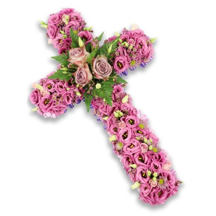 A beautifully detailed floral cross stands alone against a pure white background, its entire form composed of carefully placed blossoms in soft pink, mauve, and lilac tones. The cross appears plush and full, as if each flower has been gently pressed into place to form a comforting, petal-covered surface. At its centre, the meeting point of the vertical and horizontal arms is crowned by three fully open roses in shades of dusty rose and muted mauve. Their petals are layered and slightly ruffled, opening outward in soft curls that express tenderness and quiet devotion, much like the reflective moments shared by families leaving a service in Grove Park. Surrounding these central roses, bright fern fronds and small, vivid green leaves nestle among the blooms, offering a fresh contrast and evoking the tranquil, leafy feel of the neighbourhood. 

Extending from this focal point, the arms and base of the cross are made up of tightly grouped Lisianthus flowers. Their trumpet-shaped petals range from gentle blush pink to richer rose-mauve, some with deeper-toned centres that provide subtle variation and visual depth. Between the Lisianthus, dainty filler flowers in pale pink, cream, and soft purple are tucked in, creating small highlights that catch the light. Light green buds scattered throughout hint at renewal and the continuity of life even in moments of farewell. Along the edges of the cross, narrow glimpses of a darker purple ribbon or structural base can be seen beneath the thick layer of petals, reinforcing the cross's shape and lending a sense of craftsmanship and care. Created in the style of a traditional Christian tribute by a skilled local florist, this floral cross would be at home in a Grove Park church, crematorium, or graveside, offering a calm, dignified way to honour and remember a loved one. 