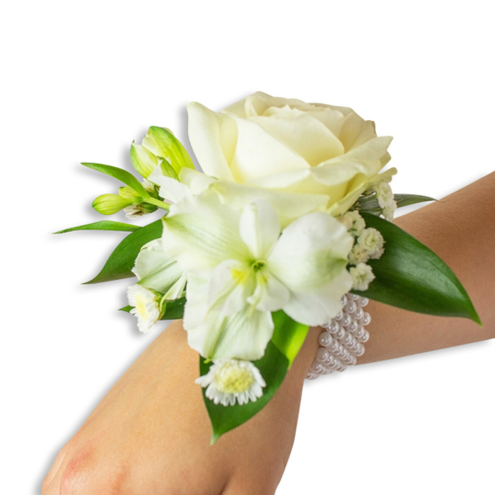 Seen from a gentle overhead angle, this fresh wrist corsage rests on a fair wrist against a crisp white studio background, presenting a harmonious study in creams, whites and deep greens. Dominating the composition is a full, creamy-white rose whose velvety petals unfurl in soft concentric layers, reflecting the soft studio light with a warm luminescence. Beneath it and leaning slightly left, a trumpet-style white bloom - likely an alstroemeria - displays delicate, slightly ribbed petals and a pale green-yellow center that creates a natural focal shift and visual depth. Scattered throughout the design are several green-tinged buds, some poised to open, suggesting a bouquet that changes over the course of an event. Feathery sprigs of gypsophila weave between the larger florals, producing a cloud-like, textural counterpoint, while a small grouping of white daisy-like florets with vivid golden cores provides a charming, nostalgic accent near the wrist. The flowers are set against broad, glossy deep-green leaves that give weight and a saturated contrast to the pristine blooms, their waxy surfaces catching highlights and framing the arrangement. The corsage is fastened by a multi-strand band of uniform white pearls; the beads are cool to the touch and lend an air of traditional elegance. This piece is created with the same attention to balance and proportion I use for local ceremonies and dances in Grove Park and surrounding areas such as Baring Road and Elmstead Woods, making it a timeless choice for brides, attendants and prom-goers seeking subtle refinement.