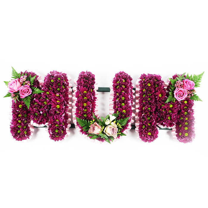 This image shows a carefully constructed floral arrangement spelling MUM in tall, capital letters, presented against a simple, pristine white backdrop that highlights every contour of the design. The letters themselves are solid and three-dimensional, with their front surfaces densely packed with countless small spray chrysanthemums in shades of deep magenta, fuchsia, and purple. The blooms are placed tightly together, creating a soft, cushion-like texture, while the discreet green centres lend a natural, garden-fresh accent throughout the tribute. Along the edges of each letter, a pale pink ruffled ribbon is wrapped and gently frilled, introducing a soft, flowing line that contrasts beautifully with the compact flowers and underlines the sense of craftsmanship. On the upper left side of the first M, a small yet striking spray of soft pink roses, some open and others still unfurling, is tucked into a bed of green fern fronds, giving the impression of a tiny garden perched on the letter. At the base of the central U, a composed arrangement of blush pink roses, creamy white blooms reminiscent of freesia, and glossy green foliage is arranged in a comforting U-shaped curve that mirrors the form of the letter, as though cradling it. The final M echoes the first, with its own cluster of vivid pink roses and ferns on the upper right, bringing a balanced, harmonious feel to the overall piece. This is the sort of personalised funeral tribute a family in Grove Park might select after speaking with a local florist, hoping to express love, respect, and a lifetime of shared memories through flowers at a funeral or memorial gathering.