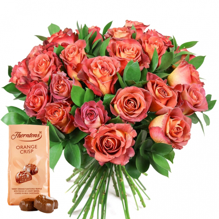 Dominating the scene is a grand bouquet of roses, crafted into a rounded mound and set against a white background reminiscent of morning light streaming into a Grove Park window. The roses reveal a gradient from fiery peach and sunlit yellow innermost petals, progressing gracefully through coral and salmon tones, and finishing with lush pink and mauve along the perimeters. Textures abound: every petal is lush and velvety, while the substantial green foliage-likely ruscus or leafy greens sourced from Grove Park Florist-provides a vibrant, living contrast to the warm floral palette. At the lower left foreground, a Thorntons Orange Crisp pouch in creamy beige stands upright, displaying its well-known logo, clear product name, and an illustration of gloss-lacquered truffles, hinting at their citrus-laced filling. Ahead of the packet, two real truffles, perfectly round and glistening, draw the viewer in. The bouquet's neatly tied stems hint at expert preparation and freshness, as if just arranged for delivery along Fauconberg Road. The entire composition feels celebratory and intimate-intended for special occasions like a Valentine's delivery near Dukes Meadows or as a gesture of gratitude within Grove Park's close-knit community. Each detail paints a story of refined taste, local craftsmanship, and the joy of giving-a distinctly Grove Park signature.