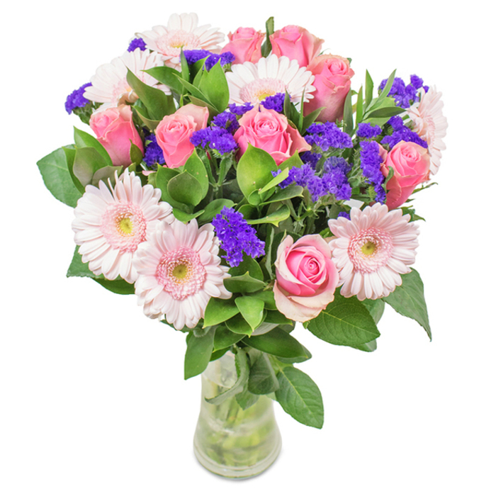 An elegantly arranged floral bouquet brims with freshness and colour, displayed within a clear glass vase and set against a bright, uncluttered backdrop-suggesting a sunlit interior in Grove Park. The centrepiece comprises about seven to nine lush pink roses, many in the early unfurling stages, their spiralling petals presenting classic beauty and softness. Interwoven are five to seven pale pink Gerbera daisies-large, round, and radiant, their centres subtly fading to near white and bringing a playful yet refined vibe to the ensemble. Bright violet clusters of statice or limonium weave a striking textural contrast, infusing deeper colour alongside the pinks. Lush, well-placed greenery cradles the bouquet from below, imparting a sense of generous abundance reminiscent of Grove Park's leafy lanes and riverside paths. The transparent vase highlights each stem submerged in clear water, underscoring the arrangement's freshness-perhaps the flowers were delivered by Grove Park Florist earlier in the day to a loved one on Burlington Lane. This bouquet, with its harmonious blend of roses, gerberas, and purple accents, is ideal for marking special moments-birthdays, anniversaries, or simply adding a note of elegance to a local Grove Park home-offering a vision of celebration, grace, and thoughtful affection.