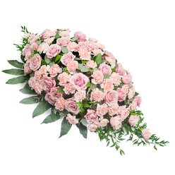 This image shows an elongated sympathy spray designed in a graceful diagonal teardrop, displayed clearly against a bright white background. The arrangement is densely packed with roses and carnations in soft, soothing shades of blush, pastel pink, and light peach, creating a blanket of colour that feels both gentle and embracing. At the wider top section, numerous fully opened roses reveal their multi-layered petals, some slightly cupped and others lying more open, their centres drawing the eye deeper into the design. Tucked between these are ruffled carnations and smaller rose blooms, which break up the smooth surfaces with their frilled edges and subtle tonal shifts. Surrounding this sea of pastel petals, rich dark green foliage offers contrast and structure, a bit like the tranquil greenery you see along the paths near the River Thames in Grove Park. Broad, substantial leaves form a supporting base around the sides, while finer, more delicate greenery trails from the narrower tip, emphasising the natural flow of the spray and creating a feeling of movement. The lighting is soft and even, bringing out the velvety texture of the petals and the polished look of the leaves without distraction. The mood is one of quiet reflection and heartfelt sympathy, suggesting that this casket spray has been created as a loving tribute for a funeral or memorial service in the Grove Park area. It appears perfectly suited to rest upon a coffin or be placed near a framed photograph, offering a silent message of comfort, respect, and lasting remembrance.