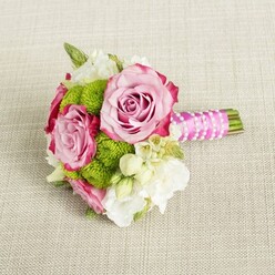 Cradled visually against a pale, textured linen-like cloth, this hand-tied bouquet feels like a moment of quiet elegance before guests arrive at a Grove Park ceremony. Three lush pink roses take centre stage, their petals unfurling in layered spirals of soft blush that deepen to a richer, almost magenta tone at the very edges. The delicate gradation of colour gives each rose depth and character, as though caught midway between bud and full bloom. Nestled among them are clusters of lime-green button chrysanthemums, tightly domed and finely textured, their tiny florets forming crisp, rounded cushions that bring freshness and a playful pop of green to the design. Around these focal blooms, dainty white and cream flowers - reminiscent of freesia or lisianthus, with a scattering of star-like blossoms that suggest waxflower - weave in and out, their small petals and yellowish centres lightening the composition and adding a sense of movement. Slender glimpses of darker green foliage add structure without overpowering the soft, romantic colours. The stems are gathered into a compact posy, trimmed neatly and wrapped in a bright fuchsia satin ribbon whose sheen contrasts with the matte texture of the fabric beneath. A fine strand of white faux pearls winds diagonally around the handle, catching the light and evoking the detail of bridal accessories. The gentle, even lighting casts no harsh shadows, allowing the shades of pink, green, and ivory to glow naturally. It's the sort of bouquet one might carry down the aisle at a Grove Park church or registry office, or order for same-day delivery from a trusted local florist to mark an engagement, anniversary, or intimate celebration at home.