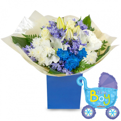 This arrangement reads like a lullaby in flowers: a tightly composed, round bouquet nestles in a deep royal blue square presentation box, the colour echoing a clear morning sky over Grove Park. At its heart, creamy white roses and poised white lilies-some buds still furled-sit among voluminous white spray chrysanthemums, creating a soft, classic foundation. Bright, electric-blue chrysanthemums punctuate the massing with confident colour, while clusters of pale lavender, hyacinth-like blooms add delicate texture and a faint, sweet perfume. Lush greenery-broad leaves with a subtle gloss and fine fern fronds-frames the blossoms and gives the arrangement depth and movement. The stems are finished with crinkled cream tissue that gathers the bouquet into a neat, gift-ready presentation. Beside the flowers a playful, light-blue foil balloon shaped like an old-fashioned pram adds a joyful note: darker-blue accents on the canopy and wheels, tiny polka dots and hearts, and the phrase "It's a Boy" in bright yellow-green announce the occasion with cheer. As a local floral designer at Grove Park Florist, I imagine this combo being chosen for a new family settling in from Baring Road or arriving at a baby shower near Chinbrook Meadows - an emblem of welcome, freshness, and careful craftsmanship, fresh enough for same-day local delivery and composed to feel both celebratory and intimately considerate.