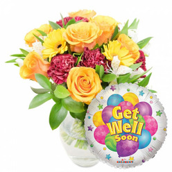 Sunlit and reassuring, this Get Well Soon arrangement reads like a gentle embrace from a trusted local florist. A generous bouquet, placed slightly left of center in a clear glass vase, features several large orange-to-deep-yellow roses with soft, velvety petals that breathe a light citrus perfume. Sunny yellow gerbera daisies add bold, open faces while deep burgundy or maroon carnations bring a plush, ruffled contrast that anchors the colour story. White alstroemeria punctuate the grouping with delicate, lily-like touches, and plentiful green foliage-glossy and crisp-wraps the blooms in a fresh, natural frame; stems and water are visible through the glass, a small testament to freshness and careful handling. Nestled to the lower right, a round silver Mylar balloon partially overlays the bouquet: a playful central design of colourful cartoon balloons in blue, purple, green, pink and yellow (some striped, some polka-dotted, some checkerboarded) dances on the metallic field. The phrase Get Well Soon appears in cheerful yellow-and-blue lettering with a soft shadow, encircled by tiny starbursts on a white rim and a discreet KALEIDOSCOPE logo at the base. As an experienced florist serving Grove Park and surrounding streets like Baring Road and Chinbrook, I would choose this combination for hospital rooms or at-home recovery because it balances brightness with tender comfort - and Grove Park Florist can arrange same-day delivery locally when needed.