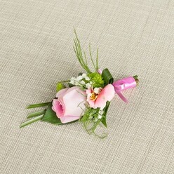 Set against a subtly textured linen, the handcrafted boutonniere tells a story of Grove Park's understated grace and the thoughtful expertise of its florists. The arrangement's heart is a tightly furled, pastel pink rose, its petals rising in a spiral of increasing softness, the outer blush echoing the gentle dawns over Chiswick House gardens nearby. A companion peachy alstroemeria opens delicately, its throat touched with yellow sunbeams and intricate markings. Dainty baby's breath and vivid green, cushion-like blooms weave through the arrangement, while fine blades of fern and broad, deep-green leaves-some smartly folded at the base-lend structure and visual intrigue. Everything is anchored by a glossy fuchsia satin bow, luminous against the neutral background. The composition is one of harmony and celebration, reminiscent of Grove Park's own community spirit, perfect for weddings at local venues or marking formal milestones. Each detail-the mixture of soft hues, crisp greens, and luminous ribbon-tells of freshness experienced in every Grove Park florist's delivery, where romance and attention to craft bloom together.