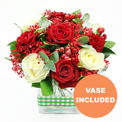 Photographed against a bright white background, this red and white rose bouquet exudes a sense of polished elegance, as if it has just been arranged in a Grove Park home ahead of an intimate dinner. At the centre of the design, full-blown deep red roses create a rich, velvety focal point, their layered petals spiralling outward with a romantic intensity. Interspersed among them are creamy white roses, soft and luminous, bringing a gentle lightness to the colour palette and highlighting the drama of the red blooms. Between the larger flowers, the florist has woven in delicate sprays of tiny, bright red filler blossoms that resemble coloured gypsophila, forming a fine, airy veil of colour that fills out the bouquet without weighing it down. Scattered clusters of glossy red hypericum berries introduce rounded shapes and a slightly deeper red tone, adding texture and a subtle festive feel, well-suited to celebrations and anniversaries delivered across Grove Park and nearby Chiswick. The flowers are cradled by fresh green foliage, including elegant eucalyptus sprigs and other rich greenery, which adds volume, depth, and a cool, herbal note to the overall look. All of the stems are arranged within a modern rectangular clear glass vase, allowing the stems to be seen and giving the composition a contemporary, uncluttered base. Around the middle of the vase, a green and white gingham ribbon is wrapped snugly, adding a touch of countryside charm that contrasts nicely with the sleek glass. In the bottom right corner of the image, a bold orange circular graphic with crisp white letters reads "VASE INCLUDED," clearly signalling that this is a complete, ready-to-place floral arrangement for effortless gifting and display in Grove Park homes.