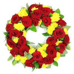 In this image, a beautifully full funeral wreath appears to float against a stark white background, its circular form defined by a rich ring of red and yellow flowers. Dozens of red roses are the main focus, each one at its peak, with velvety petals unfurling in perfect spirals. Their tones vary slightly, from true ruby red near the centre of each bloom to deeper, wine-coloured edges, creating natural shading and depth. Nestled between and around these roses, soft mounds of yellow chrysanthemums add brightness and texture, their tiny petals radiating from compact centres like miniature suns. The combination of colours suggests both profound affection and gentle gratitude, an appropriate expression of sympathy for a family gathering near Grove Park station or in one of the quiet residential streets nearby. Supporting the flowers is a layer of fresh green foliage, combining smooth, glossy leaves with some more muted, grey-green sprigs that echo the look of eucalyptus. The greenery frames the flowers without overpowering them, instead giving the wreath structure and a sense of organic movement. The circular shape is complete and symmetrical, with an open middle that conveys continuity and unending remembrance. Bright, even lighting enhances every curve and contour, highlighting the lush texture of the roses, the feathery chrysanthemums, and the subtle shine of the leaves. This carefully constructed tribute looks like it has been recently arranged on the workbench of a Grove Park florist, ready to be delivered to a local church, crematorium, or family home as a heartfelt symbol of respect, remembrance, and enduring love.