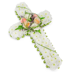 A beautifully composed funeral flower cross fills the scene, its classic Christian shape clearly defined against a pure white background that gives the arrangement a chapel-like serenity. The body of the cross is entirely made up of closely packed, white chrysanthemums, or similar small, rounded blooms. These flowers form a dense, velvety surface along the entire length and width, creating a sense of gentle softness and order. Every bloom looks freshly opened, their petals crisp and clean, evoking purity and a calm farewell. Tracing every edge is a thin border of vivid green, formed from fresh foliage and possibly tiny green blossoms. This narrow fringe of colour provides a subtle yet striking contrast with the white, emphasising the outline of the cross much like the well-tended greenery seen in gardens and along the quiet avenues of Grove Park. At the central junction of the cross, a slightly raised spray of larger flowers creates a focal point rich with feeling. Several roses in delicate shades of peach, pale apricot, soft blush pink, and creamy ivory are arranged together, their layered petals curving gently outward. They are softened further by wisps of feathery fern, loops of slender green grass, and small touches of fine purple filler flowers that thread through the composition. These hints of lavender add depth without overpowering the pastel palette. The image is evenly lit, with no harsh glare, contributing to a mood of reflection and respect. This floral cross would be ideal for honouring a loved one at a Grove Park funeral, memorial service, or graveside committal, conveying sympathy, faith, and quiet remembrance.