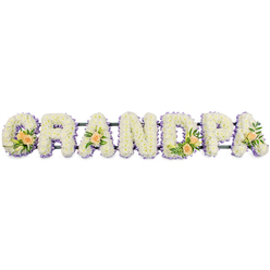 This image shows a beautifully composed floral name tribute that spells GRANDPA in prominent, three-dimensional letters, reminiscent of the pieces often displayed at funerals and memorials around Grove Park. Each letter is faced with a dense layer of fresh white chrysanthemums or similar small, multi-petalled flowers. Their tiny heads are packed tightly together, hiding the mechanics beneath and creating a plush, continuous surface that feels soft and restful to the eye. Subtle hints of yellow-green in the flower centres provide the faintest touch of colour, yet from a distance the letters appear as clean, luminous white.   

Framing each letter is a fine border of soft lilac or pale purple blooms, running evenly around the edges like a gentle outline in watercolour. This cool lavender tone contrasts lightly with the white, defining the strong shapes of the G, R, and N while softening the angles of the A, D, and P. The border contributes a sense of poise and quiet sophistication, well suited to a thoughtful farewell in Grove Park. At several points across the word - specifically at the G, first A, D, and final A - are clusters of peach roses tucked into the chrysanthemums. Some roses are budding, others just unfolding, their petals glowing in shades of creamy apricot and soft peach.   

These rose groupings are enhanced with sprigs of deep green foliage and a few slender white buds suggestive of lilies, adding depth and gentle fragrance. The letters rest on a slim, dark support bar that links them discreetly along the base, keeping the tribute steady for display on a stand or easel. Presented against a stark white background, this GRANDPA floral piece stands out as a dignified, heartfelt expression of remembrance for a beloved grandfather within the Grove Park area.