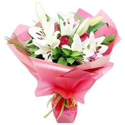 This image showcases an elegant florist's bouquet composed of snowy white lilies and deep red roses, photographed against a minimalist white backdrop so that every petal and ribbon stands out clearly. Several Oriental lilies form the focal point, their large, trumpet-shaped blooms fully open, the petals creamy white and gently recurved, with dark brown stamens stretching from pale green centres. Around them, unopened lily buds reach upward, wrapped in fresh green skins that suggest the bouquet will continue to evolve across several days. Tucked intimately between the lilies are velvety red roses, their petals packed in tight spirals, some still in bud, others slightly loosened, introducing both romance and depth. The arrangement is surrounded by an abundance of vivid greenery, where broad, rich green leaves provide structure and finer, grassy fronds curve and twist to soften the edges. All the stems are gathered together and swathed in lustrous bright pink cellophane, layered so that it flares out in translucent waves around the blooms, catching light and adding a sense of celebration. At the base, a delicate lime green ribbon is tied neatly around the stems, its satin finish and lively colour a fresh counterpoint to the pink and red. The composition feels like something carefully prepared by a local Grove Park florist for moments that matter-a Mother's Day surprise to a house near Grove Park Road, a romantic anniversary delivery to a riverside apartment, or a thoughtful gesture of appreciation for friends meeting near Chiswick Station-radiating fragrance, warmth, and genuine sentiment.