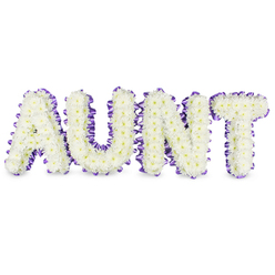 Here a personal message is made tangible: the word "AUNT" rendered in bold, uppercase letters and entirely formed from tightly clustered white spray chrysanthemums. The blooms feel almost feather-light to the eye, their small, ruffled petals creating a soft, cushion-like texture while tiny pale yellow centres offer a whisper of warmth within the white field. Each letter is bordered with a rich purple satin ribbon, carefully pleated to produce a refined ruffled edge that both outlines and supports the floral silhouette. The ribbon's sheen provides a gentle counterpoint to the matte petals, lifting the composition with a quiet dignity. Studio light washes over the tribute in a soft, even glow, revealing subtle grey shadows under the letters that suggest depth and a real-world presence on a white surface. There is a clean, green fragrance to the chrysanthemums - fresh and lightly dewy - which threads through the arrangement like a comforting memory. Made with thoughtful precision by florists accustomed to delicate commemorations in Grove Park, this piece balances sturdiness and tenderness: the letters rest on firm frames while the flowers keep a compassionate softness. Intended as a sympathetic tribute for funeral services or memorial gatherings, the design communicates respect and lasting affection, a visual embrace for grieving families. Local delivery across Grove Park and neighbouring streets is offered to make this bespoke memorial accessible to those arranging tributes close to home.