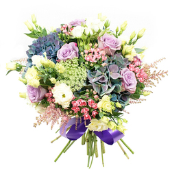 With every detail thoughtfully arranged, this lush Grove Park bouquet evokes the tranquillity of West London's hidden green corners. The eye is drawn first to the decadent hydrangeas, blooming in jewel-like shades of indigo, teal, and purple, their plush clusters suggesting early morning dew on the lawns of Chiswick House Gardens. Nestled within their embrace, soft lilac roses and creamy white blooms unfurl, each petal edged with the subtle grace of classic romance. Interspersed throughout are snow-white ranunculus, their many-layered, ruffled petals recalling the charming textures of Grove Park's springtime hedgerows. Elegant yellow eustoma buds and partially-open lisianthus reach upward, scattering pale green and soft yellow highlights through the bouquet. Vibrant sprays of fuchsia-pink filler flowers break through the cooler palette, echoing lively street markets along Fauconberg Road, while delicate pink astilbe and light, lacy Ammi Majus add airiness and intricacy. The bouquet is framed by fresh green foliage, grounding the composition like the sturdy oaks and sycamores lining local avenues. The carefully bundled stems are finished with a wide royal purple satin ribbon, its shine amplifying the bouquet's cool, celebratory tones. Perfect as a heartfelt congratulation, a birthday surprise for neighbours, or simply to brighten a home in Grove Park, this arrangement showcases the thoughtful design and botanical flair of a true local florist.