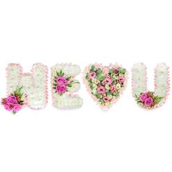 Seen close-up, the floral message H, E, a heart, and U reads like a handwritten note in blossom-white chrysanthemums form the solid letters with a pillowy, tactile surface, each edge wrapped in a pale blush satin ribbon that ripples slightly like a folded page. The designer has placed bright fuchsia roses as affirming punctuation: a vivid cluster at the left foot of the H, a bold trio across the middle arm of the E, and a small pair tucked into the inside curve of the U, their saturated colour and faint citrus-rose scent bringing warmth to the otherwise peaceful white. The heart at the centre is intentionally softer in palette and texture: layers of soft pink carnations, creamy lisianthus or diminutive roses create a romantic, layered mosaic, while pale green eucalyptus leaves are woven through to introduce cool, silvery notes and a gentle rustle if touched. Small sprays of deep red berries and slender, fern-like greenery offer contrast and help the eye travel across the design. Gentle studio lighting emphasizes the satin ribbon's sheen and the subtle shadows between petals, lending the tribute a quiet dignity. Made with the steady hand of an experienced florist, this arrangement is suited to memorials, celebration-of-life ceremonies, or as an intimate expression of love in Grove Park and neighbouring Hither Green or Lewisham-an orderly, heartfelt composition that speaks of remembrance, tenderness, and enduring affection.