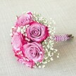 A dazzling round bouquet rests gracefully atop light, softly textured linen, its vibrant presence echoing celebration and elegance throughout Grove Park. The focal roses unfold in rich purple-to-pink gradations, their petals glowing lavender at the center and finishing in bold magenta at the ruffled edges. Intertwined with ethereal tufts of white gypsophila, the flowers create a harmonious interplay of colour and softness, reminiscent of community gardens near Fauconberg Road. The hand-wrapped satin handle, deep purple and lustrous, spirals upward with strands of iridescent pearls, offering a luxurious texture that invites closer appreciation. Fresh, neatly bundled stems peek beneath the wrap, reaffirming the bouquet's connection to nature and the florist's artisanal craft. Bathed in the warm glow of natural daylight, this arrangement is suited for Grove Park weddings, anniversary soirees, or joyful gatherings along the Thames-every detail a tribute to love, artistry, and the local spirit that flourishes in this corner of London.