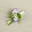 A finely detailed close-up of a single wedding boutonnière rests on a softly textured light beige linen, the neutral fabric gently lit so its subtle weave frames the flowers without distraction. At the heart of the design, two open lisianthus blooms glow in creamy white, each petal edged with a vivid band of deep purple that ripples along the ruffled contours like ink on silk. Nestled beside them are tiny clusters of pure white filler flowers, reminiscent of baby's breath, adding a cloud-like softness and giving the piece a gentle, romantic air. Threading vertically through the composition is a slender spike of densely packed muscari, its tiny bell-shaped flowers a rich grape-purple that deepens the palette and introduces a woodland charm. Around these focal elements, fine, feathery greenery, likely asparagus fern, mingles with a few slightly broader green leaves, creating a fresh, garden-picked feel that still feels refined and composed. Two pale green buds, not yet open, tilt quietly from the side, suggesting new beginnings and the unfolding of the day ahead. The exposed stems are neatly gathered and wrapped in crisp white satin ribbon, smoothed tight and finished with a small, elegant bow that signals this piece is ready to be pinned to a lapel. The overall mood is calm yet celebratory, the kind of understated elegance a groom or prom guest in Grove Park might choose for a ceremony in a local church or a reception in a nearby park venue, the floristry speaking in a soft, confident voice rather than a shout of colour.