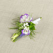 A small, intimate celebration in floral form, this boutonniere gathers the soft romance of early spring into a compact, wearable piece. Two lisianthus blooms-white at the heart with lavender-blue ruffled edges-anchor the design, their velvety petals inviting a careful touch. Tiny clusters of baby's breath nestle between them like a pale, fragrant cloud, while slim, pale buds and the vertical rhythm of grape hyacinth spikes in blue-violet introduce movement and contrast. Feathery fern fronds arc gently around the blooms, lending an airy, almost woodland texture that feels simultaneously fresh and timeless. The stems are wrapped in a neat ribbon-satin to the touch-and the boutonniere sits against a neutral linen backdrop that highlights the cool tones and subtle sheen of each petal. Under soft daylight the colours are cool and confident, the scent faint and green, a whisper of spring rather than a declaration. Designed to be pinned at a wedding, a milestone celebration, or for an intimate portrait, this piece reads as a tender, considered detail that complements both formal attire and relaxed countryside gatherings. Prepared with same-day care and an eye for balance, it travels well to venues around Grove Park, Chinbrook Meadows, and neighbouring streets, arriving fresh and composed for the moment it will be fastened and remembered.