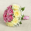 Resting on a light, neutral-toned cloth with a gently woven grain, this hand-tied rose bouquet draws the eye with its deliberate balance of colour and texture. The arrangement has a rounded, almost symmetrical shape when seen from a slightly raised angle, and is divided into two harmonising halves: deep fuchsia and magenta-pink roses on one side, creamy, soft yellow roses on the other. Each bloom is fully open, the petals spiralling outward in velvety layers that suggest both luxury and tenderness. Fine sprays of white baby's breath are intricately threaded among the roses, creating delicate, cloud-like pockets of white that add softness and a lace-like finish. Just beneath the blossoms, rich green leaves appear in small glimpses, adding depth and giving the bouquet a grounded, natural look, much like the greenery that lines the calm residential streets and riverside walkways around Grove Park. The stems are gathered neatly, bound into a sturdy handle that is wrapped in shining pink satin ribbon, its surface smooth and reflective. Twined around this ribbon is a slim strand of tiny white pearls, turning in an elegant spiral from top to bottom, echoing the traditional elegance of bridal accessories. The light falling across the bouquet is soft and diffuse, enhancing the sense of romance without casting harsh shadows. Perfect for a wedding, engagement, or anniversary celebration in Grove Park and the surrounding W4 area, this bouquet feels both timeless and personal, as though it has been designed specifically to be carried, cherished, and remembered in photographs for years to come.