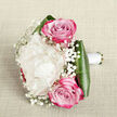 Photographed from just above, this intimate bouquet lies on a background of softly folded, off-white fabric, the subtle texture of the cloth echoing the natural fibres of linen and setting a calm, elegant tone. At its centre blooms a single, sumptuous creamy white peony, generously ruffled petals overlapping in layers that billow outward like a small cloud, instantly drawing the eye. Framing this focal flower are two vivid pink roses, placed one slightly above and one below, their tightly wound centres spiralling inward while the petals shift from gentle blush at the base to rich magenta along the outer edges, adding both romance and depth. Fine, branching sprays of white baby's breath are threaded through the arrangement, each tiny blossom like a speck of snow, creating an airy veil that softens the transitions between the larger blooms. The base of the bouquet is embraced by broad, glossy dark green leaves, which curve around the stems to provide structure and a deep, grounding contrast against the light petals and neutral fabric. A smooth white satin ribbon encases the stems, neatly wrapped to form a graceful handle that suggests this bouquet has been crafted to be held, perhaps by a bride walking from her Grove Park home to a nearby ceremony or given as an intimate anniversary gift. Soft, natural light in the photograph highlights the peony's velvety texture and the subtle sheen on the foliage, while gentle shadows lend dimension. The overall composition feels romantic, fresh, and quietly sophisticated, the sort of thoughtful floral design a Grove Park florist might create for same-day delivery when love and celebration are the focus.