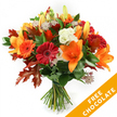 A hand-tied, autumnal bouquet stands upright against a crisp white backdrop, a carefully balanced study in warm tones and seasonal texture. The composition centres on open, trumpet-shaped orange lilies with visible stamens and a few tight buds promising more bloom; around them, plump Gerbera daisies in ruby red and vivid orange form cheerful, circular faces. Creamy white Lisianthus with softly ruffled petals slip between the bolder blooms, lending a cool, delicate contrast, while star-like Astrantia in dusky purple-pink threads its filigree into the arrangement, catching light and adding a faintly whimsical texture. Deep green foliage-likely ruscus or salal-creates a lush base that grounds the colours, and the arrangement's autumn identity is confirmed by several large, deeply lobed oak leaves in varying shades of burnt orange and reddish-brown, their crisp veins and irregular edges giving the bouquet a natural, woodland silhouette.
Stems are neatly gathered and bound with dark twine or raffia, the visible finish signalling a traditional hand-tied technique and the fresh-cut quality of the flowers. The lighting is soft and even, emphasising petal surfaces, the satin sheen of lilies, and the velvety richness of the gerberas without harsh shadow. In the lower right corner a bright orange diagonal banner overlays the image with the bold white text FREE CHOCOLATE, a clear promotional overlay. This arrangement radiates warm hospitality-perfect for autumn birthdays, a Thanksgiving table, or as a thoughtful delivery to brighten a neighbour's day in Grove Park or nearby streets-conveying the scent of green stem and gentle sweetness that lingers after a bouquet is set down.