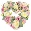The photograph presents a lush, heart-shaped wreath of pastel flowers set against a smooth white background, as if floating in soft light. The heart is fully defined and carefully filled, with no gaps, giving it a feeling of completeness and devoted attention. Creamy ivory and pale yellow roses serve as the main focal blooms, their tightly layered petals forming rounded, elegant shapes that draw the eye and suggest calm, enduring affection. Between these roses, numerous clusters of ruffled light pink carnations create a gentle, cushion-like texture, their frilly edges overlapping in soft waves. Deeper tones of magenta and mauve-pink lisianthus are interspersed throughout, their more open, trumpet-like flowers adding nuance and a hint of romantic intensity to the otherwise gentle colour scheme. Silvery-green eucalyptus leaves weave in and out of the flowers, their smooth, rounded foliage offering a cool contrast and helping to define the heart's curve. Tiny yellow-green buds appear here and there, suggesting fresh blooms on the verge of opening and bringing a quiet sense of life and renewal. The wreath has a serene, contemplative presence, the kind of arrangement families in Grove Park might choose to accompany a farewell service, whether in a local chapel or at a riverside memorial. It speaks of sympathy, remembrance, and the soft comfort of shared memories, offering a visual expression of love and loss that feels both personal and refined. The simplicity of the background ensures that all attention remains on the flowers themselves and the emotions they convey.