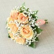 Set against a soft, textured background evocative of Grove Park's local charm, this bridesmaid bouquet shines with understated elegance. At its heart, seven to eight roses in shades of peach and apricot unfold their petals in floral harmony, each bloom expertly positioned for maximum beauty and balance. Clusters of white baby's breath are scattered throughout, adding a whisper of airiness and contrast reminiscent of the cloud-like blooms often found in Grove Park's green spaces. Rich, deep green leaves provide depth, anchoring the arrangement and enhancing the roses' gentle warmth. The bouquet is shaped in a classic round, hand-tied fashion, reflecting meticulous attention to design. Stems are gathered in a satin ribbon of coral-peach, elegantly wrapped and adorned by a spiraling line of faux pearls that add a touch of sophistication and luxury. The ends of the stems emerge neatly at the base, evidence of the bouquet's fresh, just-made quality. Bathed in even, natural light-like that which filters through the windows of Grove Park's community halls-the bouquet's colors and textures flourish, each detail crisp against the subtle linen. Whether held by a bride or bridesmaid along the leafy streets of Grove Park, or gracing the table at a local gathering, this bouquet captures both the beauty of floral artistry and the heartfelt spirit of the SE12 neighbourhood.