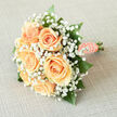 There is a hush of spring in this hand-tied bouquet: peach roses gathered tightly at the heart, their petals layered in creamy spirals that seem to glow from within when caught by soft daylight. Encircling these roses, a frothy veil of white gypsophila floats like a gentle mist, each tiny blossom softening edges and amplifying the bouquet's sense of innocence. Shiny, emerald-green foliage supplies depth and a cool counterpoint to the warm peach tones, allowing each rose to read clearly even from a distance. The stems are wrapped with peach satin, the fabric smooth under the fingers, and secured with a single, graceful string of pearls that adds a classic, tactile finish-pearls that flicker quietly in photos taken on leafy streets or outside the cafés near Grove Park station. The scent is subtle and fresh: the delicate green perfume of roses rather than heavy headiness, conjuring images of morning light on garden paths and the quiet green of Grove Park Nature Reserve. As an experienced local florist, I picture this bouquet accompanying brides walking past familiar neighbourhood landmarks or resting as a cherished keepsake after an intimate celebration. Created with careful technique and an eye for balance, it's suited to weddings, anniversaries, or refined table settings across Grove Park, Lee and Hither Green. (Grove Park Florist prepares and dispatches hand-tied bouquets for local occasions and photos in the area.)