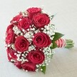 A striking statement of passion and elegance, this Grove Park bouquet encases tradition and modernity in every detail. Lavish, deep red roses-a dozen and more, fully open and richly textured-create a plush, round heart, surrounded and softened by a lavish scattering of crisp, white baby's breath. The effect is airy, romantic, and lush, with tiny blooms floating among the substantial roses. Hints of vibrant, dark green leaves peep through, grounding the color palette in the natural beauty reminiscent of Grove Park's riverside parks and leafy lanes. The stems are grouped tightly, the gathered base dressed in a wide red satin ribbon-slick and sumptuous, glinting in the light-accented with elegant horizontal white stripes and a whimsical spiral of luminous pearls. Resting on a pale, gently textured background, the bouquet shimmers under soft lighting, every element clear and full of life. Crafted with care by Grove Park Florist, this bouquet is ideal for weddings at nearby St. Michael and All Angels, memorable anniversaries, or any intimate celebration. Its harmonious balance of vivid color, refined finishing, and classic flower symbolism-red roses for true love, baby's breath for lasting innocence-makes it a beloved choice for those looking to celebrate romance right here in Grove Park, with freshness guaranteed for timely delivery.