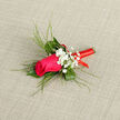 This wedding boutonnière showcases a single magenta rose at full, poised perfection, its velvety petals layered in a generous spiral that draws the eye straight to the heart of the bloom. Surrounding it is a collar of lush green leaves, paired with fine, arching blades of foliage that curve outward to create a gentle, sculptural frame, as serene as the leafy paths running towards Grove Park station. Interwoven between the greens are clusters of white baby's breath, each tiny bloom forming part of a soft, airy veil that offsets the bold colour of the rose and brings a note of classic romance. The stem is meticulously wrapped in a vivid red ribbon, wound in smooth, even coils with no loose edges, its lustrous finish adding a festive flourish that hints at toasts and laughter later in the evening along the riverside by Strand-on-the-Green. Resting against a neutral, textured fabric background, the boutonnière appears crisp and thoughtfully balanced, with every element carefully proportioned: the upright rose, the delicate gypsophila, the structured greenery, and the clean line of ribbon. You can almost sense a gentle fragrance-sweet rose layered with fresh, grassy notes-ready to accompany the wearer from the first quiet moments of getting dressed to the final farewell at a Grove Park celebration. Crafted with practiced hands, this floral piece speaks of care and intention, perfect for a groom, best man, or special guest who wants a subtle yet striking accent that will appear beautifully in photographs and remain memorable long after the day has passed.