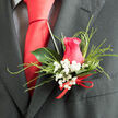 Composed with the practiced ease of a local Grove Park florist, this wedding boutonnière is a delicate study in contrast and feeling. The focal point is a beautifully shaped hot pink rose, its petals plush and velvety, cupping around one another as though protecting a secret at the centre. The colour sits confidently between raspberry and fuchsia, vibrant enough to draw the eye in wedding photos taken along Grove Park Road or by nearby riverside paths. Around the rosehead, fine clusters of white baby's breath gather like a soft mist, their tiny blossoms forming a cushion of lightness that tempers the intensity of the pink. Slender, feathery blades of decorative grass arc around the design, creating fluid lines that suggest movement, as if stirred by a breeze drifting off the Thames. Behind the flowers, a single glossy green leaf lends structure, its gently curved form and subtle sheen offering a calm, natural backdrop. At the base, a thin red ribbon is wrapped carefully around the stems and finished in a discreet bow, the satin catching the light with a restrained gleam, signalling careful craftsmanship rather than showiness. Pinned to the lapel of a dark, sharply cut suit, the boutonnière appears fresh and composed, a small but meaningful accent designed for a groom, best man, or honoured guest. It feels like a floral expression of warmth and commitment, suited to intimate ceremonies in Grove Park churches, elegant receptions in Chiswick, or any special gathering where a carefully chosen rose can say what words sometimes cannot.