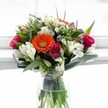 This radiant bouquet, thoughtfully composed by Grove Park Florist, embodies the freshness of spring mornings along Chiswick's garden-filled lanes. Anchored by a vibrant orange gerbera daisy whose bold petals invite immediate cheerfulness, the arrangement is embraced by luxurious magenta and deep crimson roses-some fully blooming, others tightly furled with a sense of promise. Among these, white alstroemeria, their petals streaked and gently spotted, curve outward like graceful swan necks, while petite daisy chrysanthemums provide delicate, feathery texture. Creamy white and light yellow roses emerged at the top, adding soft, sunlit highlights reminiscent of an early walk through Grove Park. Wisps of lavender create gentle undertones, infusing the colour palette with graceful calm. Sweeps of polished broadleaf greens and slender, upright leaves envelop the bouquet, creating a striking frame; beneath, the carefully cut stems are visible through a crystal-clear cylindrical vase, water sparkling with purity and reflecting local craftsmanship. Drenched in natural light, this bouquet feels joyous and uplifting-perfect for celebrating milestones, sharing congratulations, or simply bringing a touch of emotional warmth to any home in Grove Park. Every detail reflects a florist's devotion and the friendly spirit of this west London community.