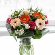A harmonious blend of colour and texture, this bouquet captures the cheerful spirit of Grove Park with every stem and petal. At its core, radiant orange and creamy peach gerbera daisies evoke the energy of spring mornings spent near Chiswick House Gardens, while velvety magenta roses thread through the display, adding touches of passion and elegance. White alstroemeria and dainty spray roses dot the arrangement, their crisp tones contributing a feeling of openness and renewal. Subtle blush pink and tiny white filler blooms nestle between larger flowers, offering layers of softness and interest. The ensemble is cradled by generous, glossy green aspidistra leaves, artistically shaped to frame the blooms in a lush embrace, reminiscent of the well-tended greenery throughout Grove Park. Tucked between the blossoms are sprigs of slender, pointed foliage that enhance the bouquet's freshness and depth. All of this beauty is gathered in a tall, transparent glass vase, where the stems are clearly displayed, rising above a softly glowing background that allows each colour to sing. The design is perfect for uplifting a space, marking a personal milestone, or conveying warm gratitude in true Grove Park style.