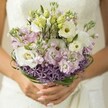 Like a whispered promise on a Grove Park morning, this bridal bouquet radiates warmth and gentle celebration. Ivory Lisianthus, their petals unfurling in soft waves, hold the tender light, mingling with pastel pink and lavender stock blossoms reminiscent of the first blooms lining Grove Park's tranquil gardens. Slender Lisianthus buds and woven bear grass add a touch of movement-an organic structure that flows, echoing the verdant rhythm of the neighbourhood's lush scenery. Anchoring it all, the spiky, violet starbursts of Allium stand bold at the base, balancing the bouquet with artistry and flair that suggests both tradition and modernity. The bride's hands, nails painted a demure rose or nude, embrace the stems just above the partially seen, expertly wrapped bouquet base, while an ivory or white lace dress glimmers out of focus behind, ensuring the flowers remain at the heart of the image. The overall effect is one of freshness, affection, and local charm-an arrangement born from Grove Park's spirit, capturing a sense of hope and timeless romantic joy.