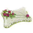 A pillow-shaped sympathy tribute, presented on a clean white backdrop, made to evoke quiet comfort and peaceful memory as seen in many Grove Park funeral chapels. The soft rectangular cushion is entirely covered with hundreds of small, pristine white chrysanthemum florets, their tightly packed petals forming a cloudlike, tactile surface that suggests calm and purity. Around the base a neat scalloped trim of folded lime-green satin ribbon creates a subtle ruffled edge, adding a gentle pop of colour and a refined frame to the white field. In the upper left corner an artful cluster of deep magenta roses, velvety and fully opened, is punctuated with tiny white freesia or lisianthus blooms; the contrast of rich rose petals against the white chrysanthemums draws the eye and offers a tender focal point. Fern fronds and glossy green foliage sit beneath and between the blooms, their feathery texture and emerald tones grounding the arrangement like a quiet garden border. Two long, arching blades of bright green bear grass sweep across the pillow, their graceful curves guiding the gaze from the top cluster toward a single matching magenta rose placed thoughtfully near the lower right - a deliberate balance that suggests solace and continuity. The composition is softly lit, catching the velvety sheen of the roses and the delicate shadows between chrysanthemum petals, and the overall effect is one of respectful serenity. As a sympathy piece often chosen for services in Grove Park or nearby chapels by the station and nature reserve, it speaks of restful sleep and a loving farewell, both elegant and consoling in tone.
