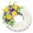 A carefully composed circular funeral wreath, shaped like a gentle 'O', rests against a plain white background, its visual language one of quiet respect and comfort. The main body of the wreath is densely built from hundreds of small, pristine white spray chrysanthemums - each tight, multi-petaled bloom pressed close to its neighbour so the surface reads almost like a soft, clouded cushion. The white petals carry a subtle satin sheen under soft lighting, suggesting delicate coolness and calm when held. Crowning the upper left curve is an elegant, asymmetrical spray of colour: several fully opened bright yellow roses, their petals spiralled from butter to deep gold and offering a faint warm scent that evokes late summer light. Interwoven with those roses are rich, royal purple lisianthus (Eustoma) with velvety, ruffled cups and a few lighter lavender buds just beginning to unfurl, giving the cluster natural depth and a feeling of life unfolding. Fresh green foliage - glossy rounded leaves, some with pale variegation, and slender fern fronds - frames the flowers, their textures ranging from waxy to feathery and lifting the colours visually. A narrow dark-purple mesh or crinoline ribbon peeks subtly from beneath the white chrysanthemums along both inner and outer edges of the ring, echoing the lisianthus tone and adding a discreet, refined edge. The open centre of the wreath reinforces the traditional circular form. This composition radiates solemn beauty and peaceful remembrance, crafted with the calm care of a neighbourhood florist accustomed to making tributes for memorials and funerals in the Grove Park area.
