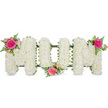 In this image, a beautifully composed funeral flower arrangement spells the word MOM in bold, capital block letters, carefully set against a bright white background so that the structure and colours are clearly defined. Each letter has been thoroughly covered in dense clusters of small white blooms, most likely chrysanthemums, whose compact, rounded flower heads create a thick, plush surface that feels soft and comforting to the eye. The white petals form a continuous blanket, conveying innocence, peace, and a respectful farewell. Underneath the floral covering, a dark green support bar and framework connect and steady the letters, adding a neat, contrasting line of colour that hints at the practical craftsmanship behind the design, just as the greenery around Grove Park quietly frames everyday life. Three coordinated clusters of coloured flowers and foliage break the expanse of white with warmth and tenderness. On the upper left of the first M, a striking fuchsia rose opens among blush-pink roses and light, feathery fern fronds, their green tips reaching slightly beyond the outline of the letter. Another similar cluster rests in the lower area between the O and the final M, gently drawing attention to the heart of the word. The last cluster, placed on the upper right of the second M, mirrors the first, creating a balanced flow of colour from one side of the arrangement to the other. The design exudes quiet dignity and affection, making it an appropriate choice for families in Grove Park who wish to express enduring love and remembrance for a cherished mother during funeral services, memorial gatherings, or graveside tributes.