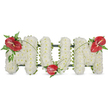 A dignified three-dimensional floral tribute spelling the word MOM in large, freestanding letters, photographed against a clean white background. Each letter is completely covered in hundreds of small, pristine white spray chrysanthemums, their tight, cushion-like heads packed so closely they form a soft, clouded surface that reads as calm and pure. The chrysanthemums give a gentle matte texture under soft daylight, the tiny petals catching light to create a whisper of shadowed depth across each curve and angle. Breaking the white with a vivid, reverent note are three glossy red anthuriums; one sits on the top left curve of the first M, another is nestled at the base of the central O, and a third blooms on the top right of the final M. Each anthurium shows its distinctive white-to-yellow spadix and a polished, almost waxy sheen that contrasts with the chrysanthemums' softness. Clusters of dark green foliage - feathery fern fronds, broader leaves and thin, arching blades of grass - frame each red focal point and trace a gentle line across the letters, visually linking the three accents and adding movement to the composition. A subtle dark green structural framework peeks out along the letter edges, giving the piece solidity and a clean outline against the white backdrop. This arrangement reads as a classic, respectful sympathy tribute for a mother, offering quiet dignity and love; it is the kind of piece a local florist would prepare for a funeral service, wake or graveside at nearby Grove Park cemetery or a chapel near Grove Park station, where neighbours and family might gather to remember with grace.