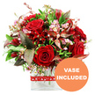 A romantic dome of red blooms is captured against a luminous white background, the kind of luxurious bouquet that feels perfectly at home in a Grove Park sitting room on a special evening. At its heart are several velvety red roses, their petals rich and deep, some still wrapped close in tight spirals, others opening generously to reveal beautifully layered centres. Interwoven among the roses are smaller deep crimson flowers, similar in spirit to alstroemeria or other multi-petalled varieties, that add texture and visual rhythm while maintaining a unified, passionate palette. Fine sprays of tiny pale pink and white filler flowers, much like waxflower, are scattered throughout the design; their slim stems and miniature starry blossoms lend an ethereal, lace-like quality that softens the intensity of the reds and creates a sense of gentle movement. The bouquet is framed by a lush collar of greenery, with fresh green leaves in varied shapes providing a vibrant, natural backdrop. Punctuating the foliage are distinctive burgundy and reddish-brown leaves, some delicately veined, which deepen the overall colour scheme and lend an air of sophistication and quiet drama. The entire composition is arranged in a clear rectangular glass vase, its modern lines and transparent sides showcasing the tidy stems and clear water within, perfect for display on a dining table or hallway console anywhere from Grove Park station to the leafy streets near the river. Encircling the vase is a red ribbon decorated with a repeating motif of small white hearts, subtly underlining the romantic intention behind the gift. In the lower right corner of the image, a bright circular orange emblem bears the phrase VASE INCLUDED in bold white capital letters, indicating that this arrangement arrives as a complete, ready-made display. The overall impression is one of warmth, love, and carefully curated elegance.