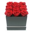 A serene studio-style photograph showcases a chic rose arrangement that feels perfectly at home in the tranquil streets of Grove Park. At the heart of the image is a square, matte black box, its surfaces smooth and velvety to the eye, its corners sharply defined. A slim, bright white band encircles the lower part of the box, adding a refined hint of contrast that reinforces the design's modern minimalism. Filling the entire opening of the box are twelve rich red roses, arranged in a flawless three-by-four pattern. Each rose is captured at the ideal moment of full bloom, with densely layered petals spiralling inward in soft, velvety folds. The crimson colour is deep and saturated, hinting at preserved or eternity roses that hold their beauty for months, if not longer. The blossoms are so closely grouped that their petal edges nearly overlap, creating a continuous cushion of red that rises just beyond the rim, giving the piece a sense of abundance without any greenery or filler. The arrangement is set against a bright white background, free from distraction, with gentle, even lighting that defines the roses' curved forms and the box's clean geometry through the softest of shadows. The mood is intimate yet composed, like a personal love note delivered in floral form to a Grove Park doorstep near Chiswick Station or along Burlington Lane. It suggests occasions filled with meaning - anniversaries, romantic milestones, or a quiet expression of gratitude - where the sender seeks a floral gift that blends contemporary design with the timeless symbolism of red roses and the reassurance of thoughtful local craftsmanship from Grove Park Florist.